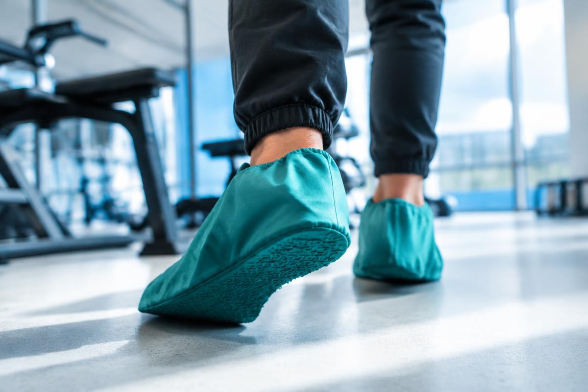 Teal shoe covers stepping onto a bright gym floor